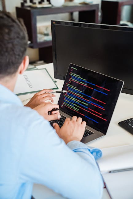 A laptop computer positioned on a desk displays a webpage with lines of code in various colours alongside a large, simple calculator interface featuring orange buttons for numeric and functional opera